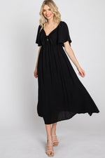 Woman models a black ruffle sleeve midi dress with a front tie detail, looking elegant.