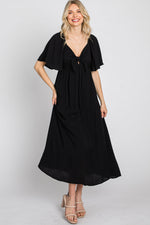 Woman models a black ruffle sleeve midi dress with a front tie detail, looking elegant.