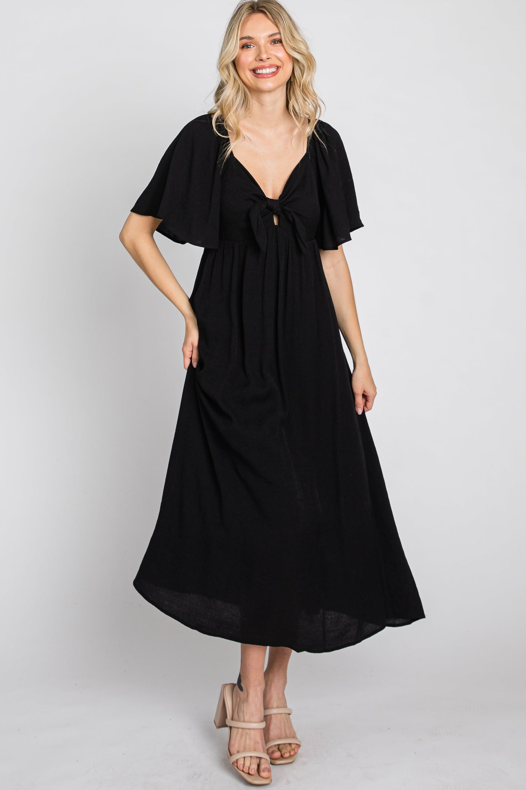 Woman models a black ruffle sleeve midi dress with a front tie detail, looking elegant.