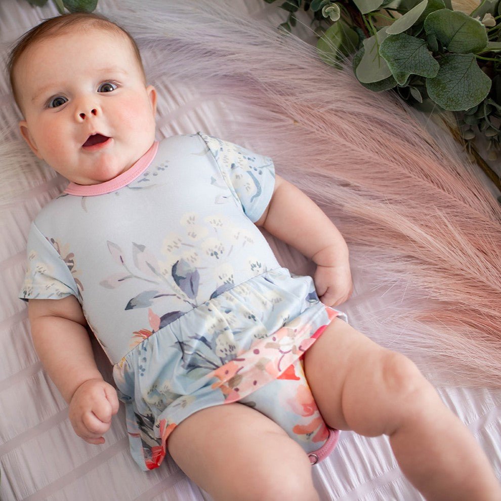 Pink blossom-print bodysuit dress with short sleeves and a ruffled skirt on a baby