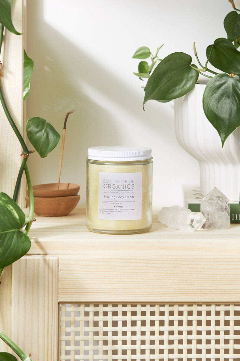 Organic body cream jar on a wooden shelf, surrounded by greenery and crystals.