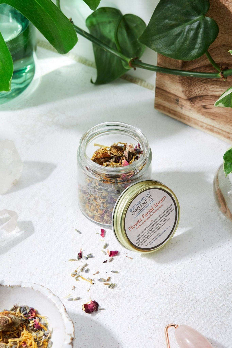 Calming Healing Facial Steam jar with dried herbs placed on a white surface, surrounded by green plants.