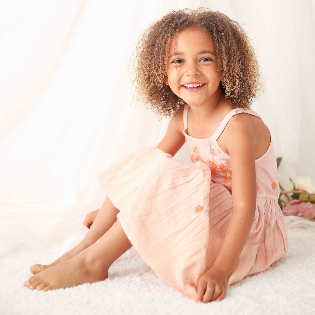Pink dress with embroidery on the top and a round neckline, worn by a child.