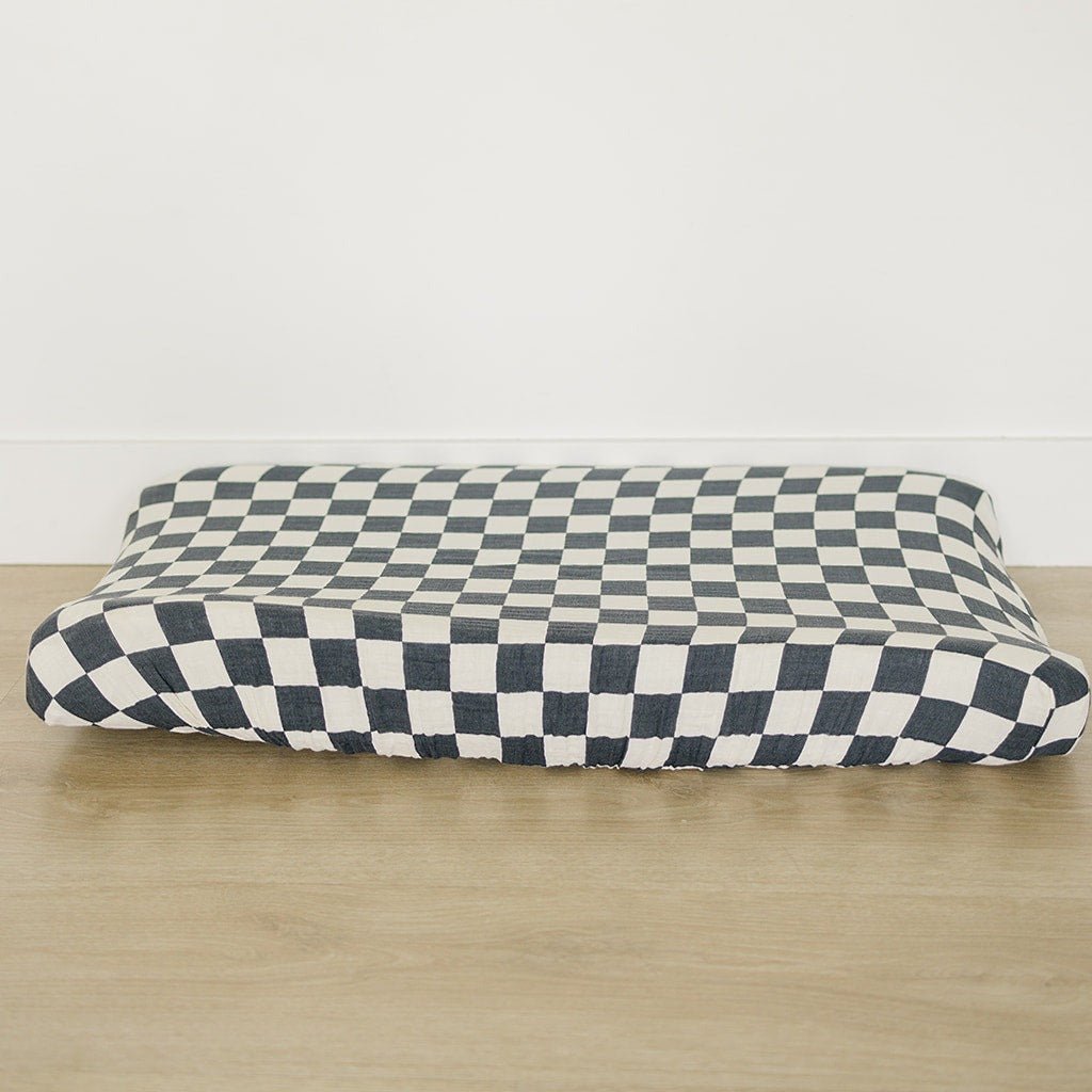 Changing pad cover in charcoal and gray checkered muslin fabric with elasticized edges fitted on a changing pad.
