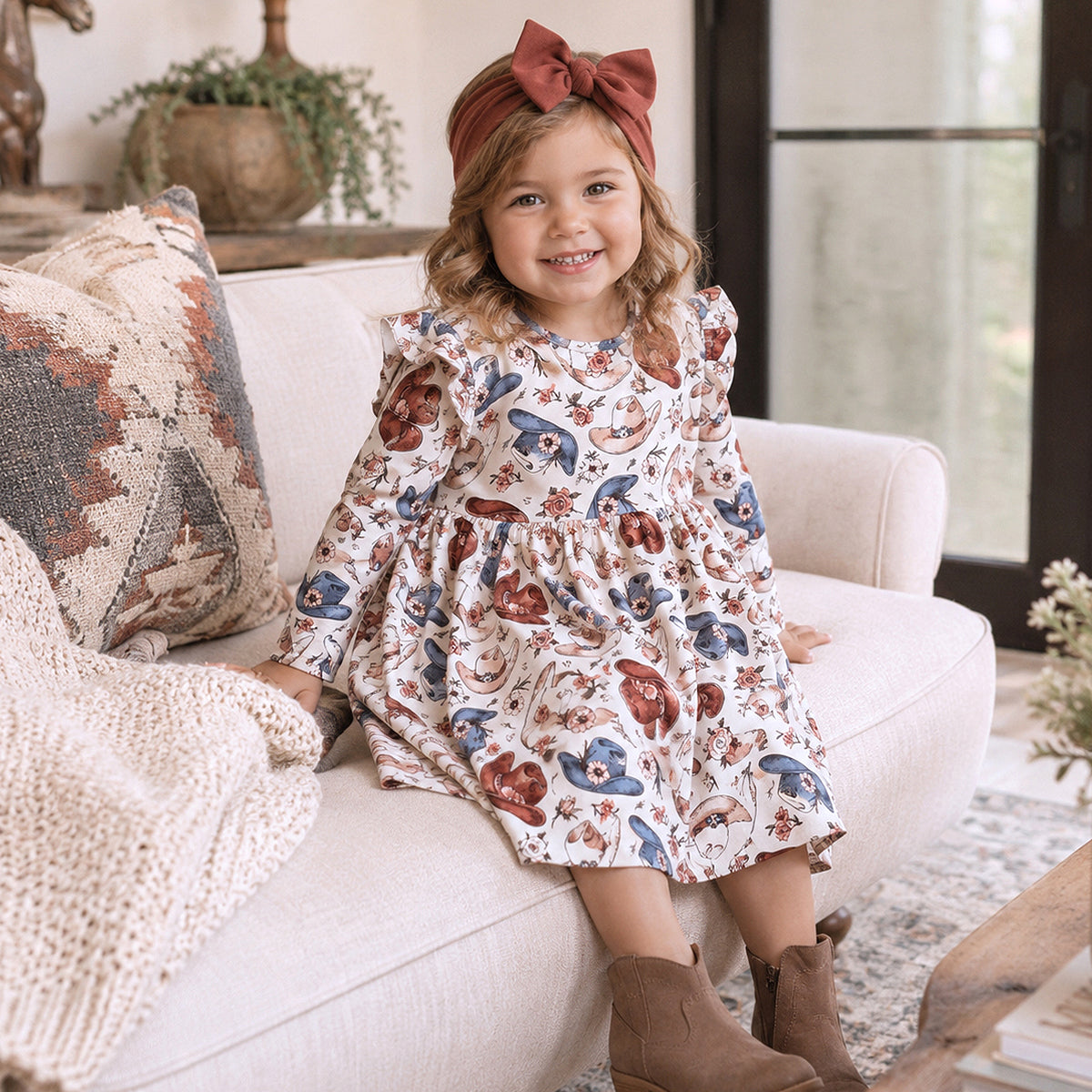 Cowgirl twirl dress with cowboy hat and floral print, ruffle-trimmed sleeves, gathered skirt, and button-back closure.