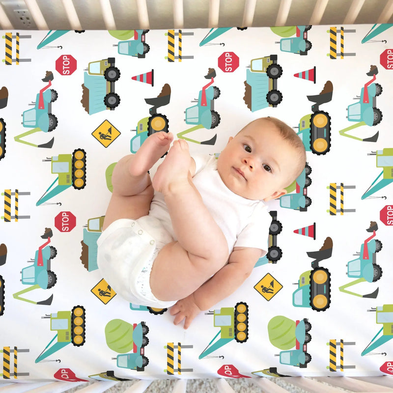 Fitted crib sheet with construction trucks pattern featuring a baby lying on it.