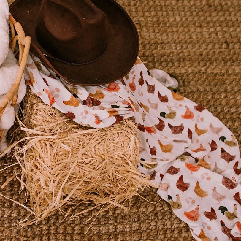 Bamboo baby swaddle blanket with a cozy chicken-and-coop themed print, spread flat