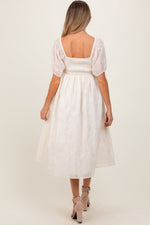 Cream maternity midi dress with delicate floral embroidery, puff sleeves, and a comfortable fit.