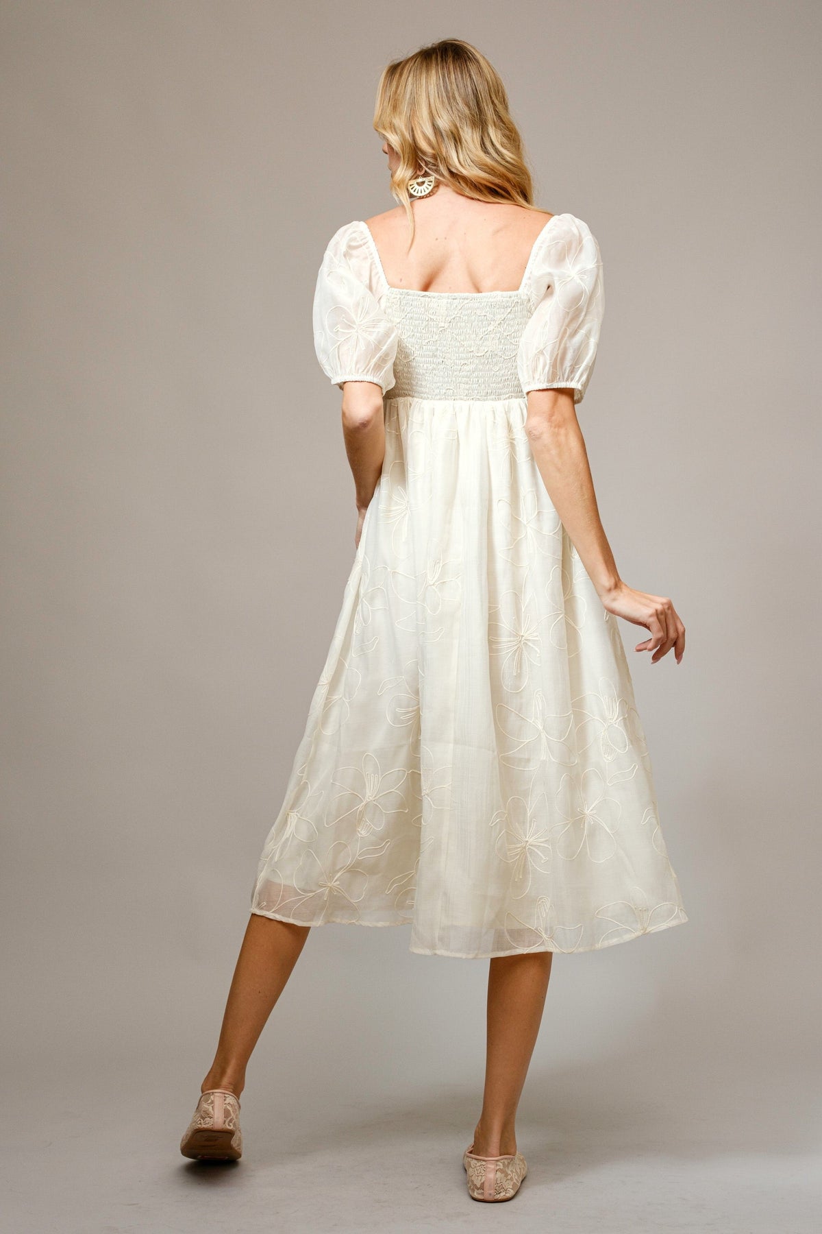 Happy baby wearing a cream organic cotton dress with floral embroidery and puff sleeves.