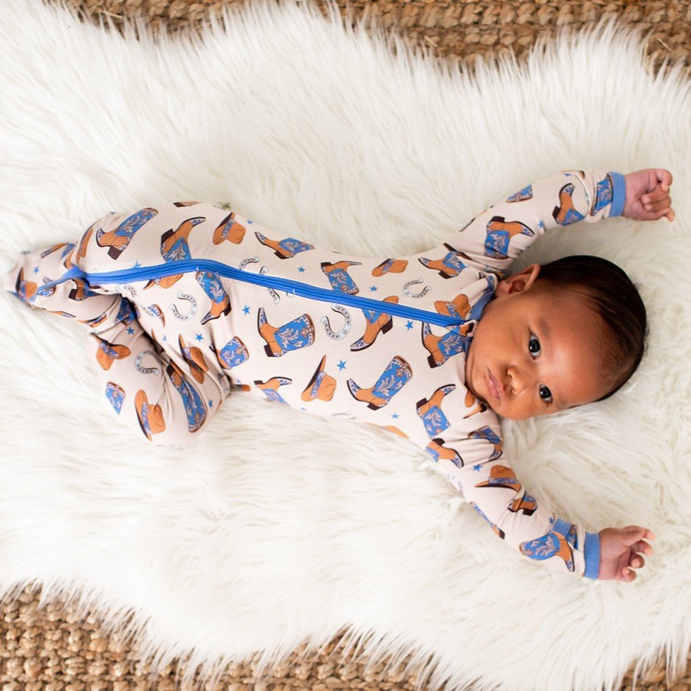 Baby footie pajamas in a light tone with an all-over western cowboy boot print and full-length front zipper.