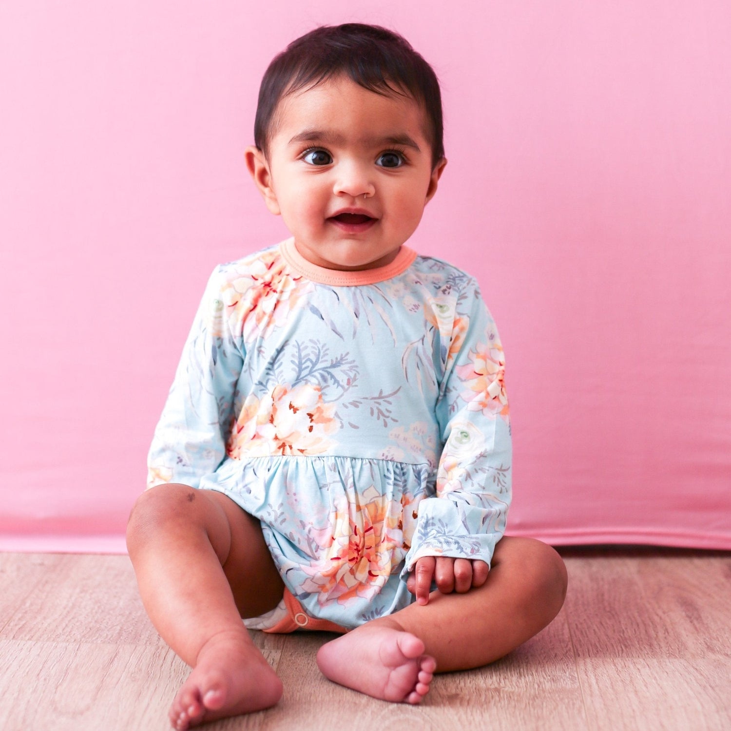 Dahlia bodysuit dress with long sleeves in a floral pattern, worn by a baby
