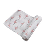 Baby wrapped in a white Newcastle Classics muslin swaddle with a vibrant dancing flamingo pattern.