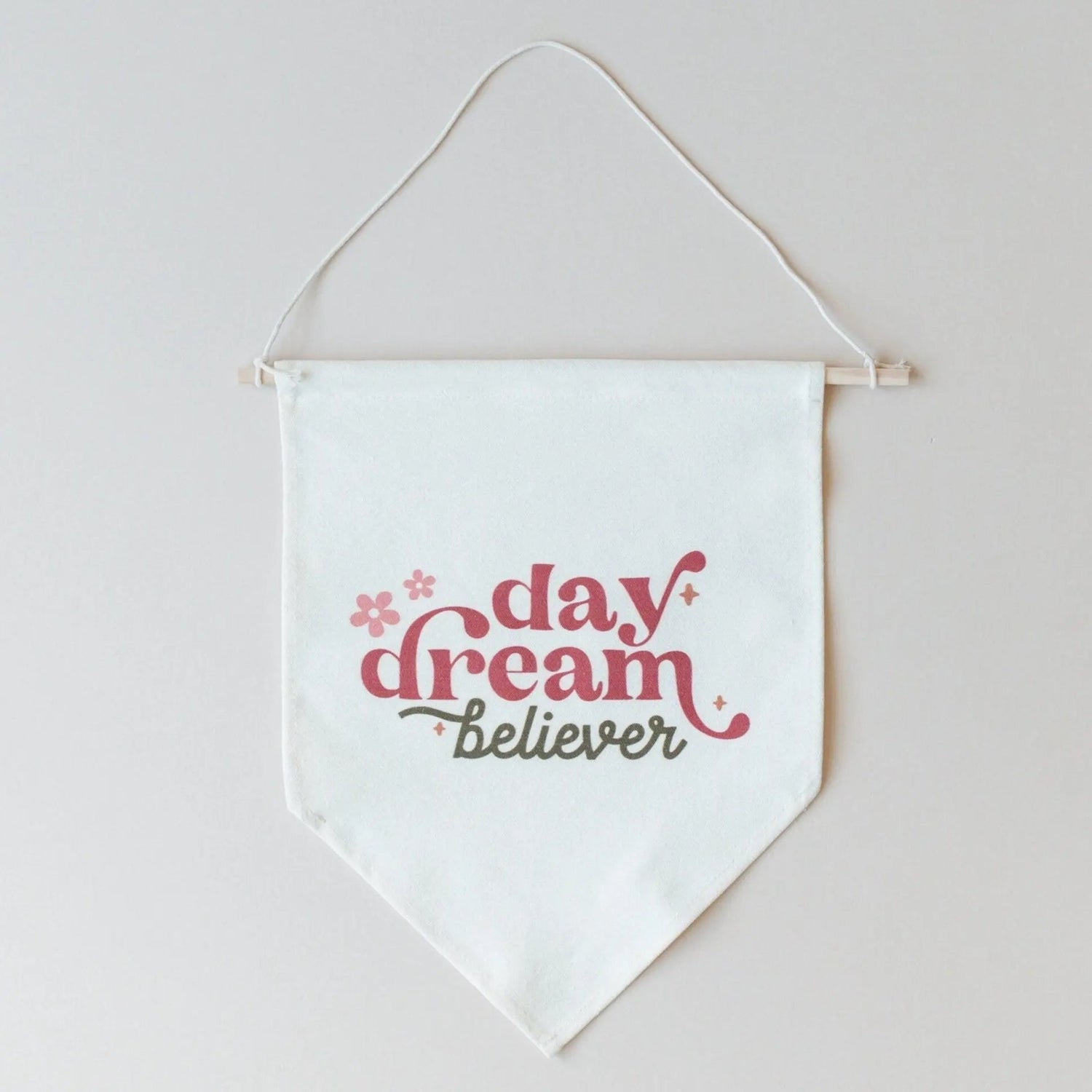 Natural-colored canvas pennant banner on a wooden dowel reading Day Dream Believer in pink lettering