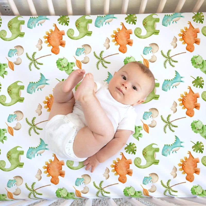 Fitted crib sheet with colorful dinosaur pattern, featuring a baby lying on the soft fabric.