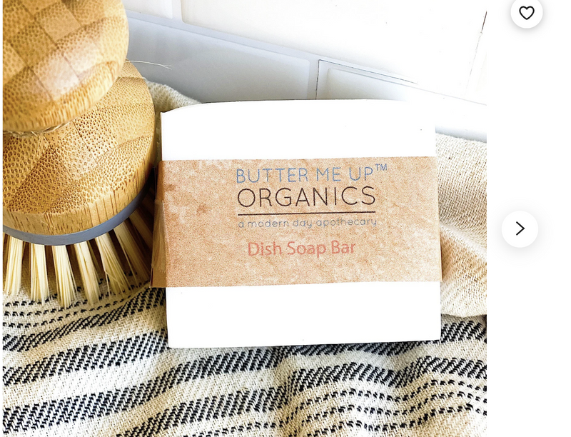 Organic solid dish soap bar from Butter Me Up Organics next to a wooden dish brush, placed on a striped cloth.