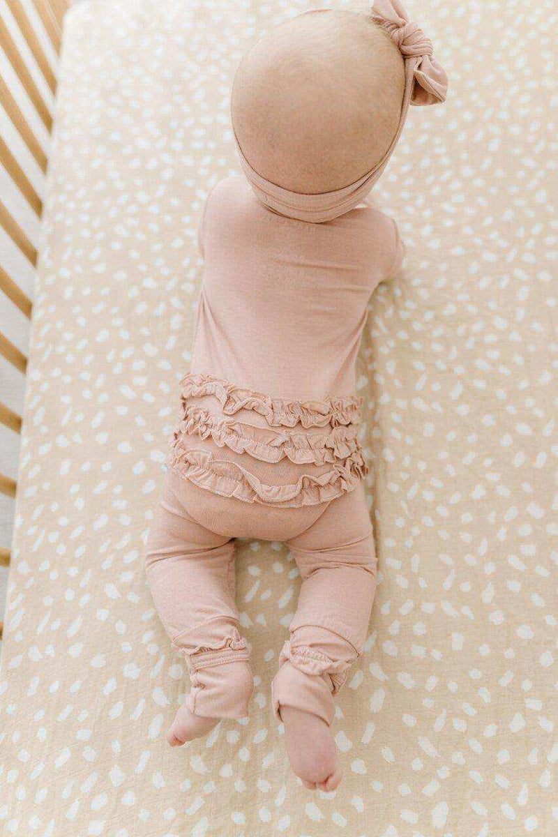 Dusty pink ruffle zipper one piece for babies with bamboo viscose fabric on a crib.