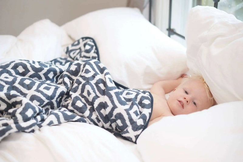 Newcastle Classics Moroccan Blue Cotton Muslin Blanket wrapped around a child on a bed.