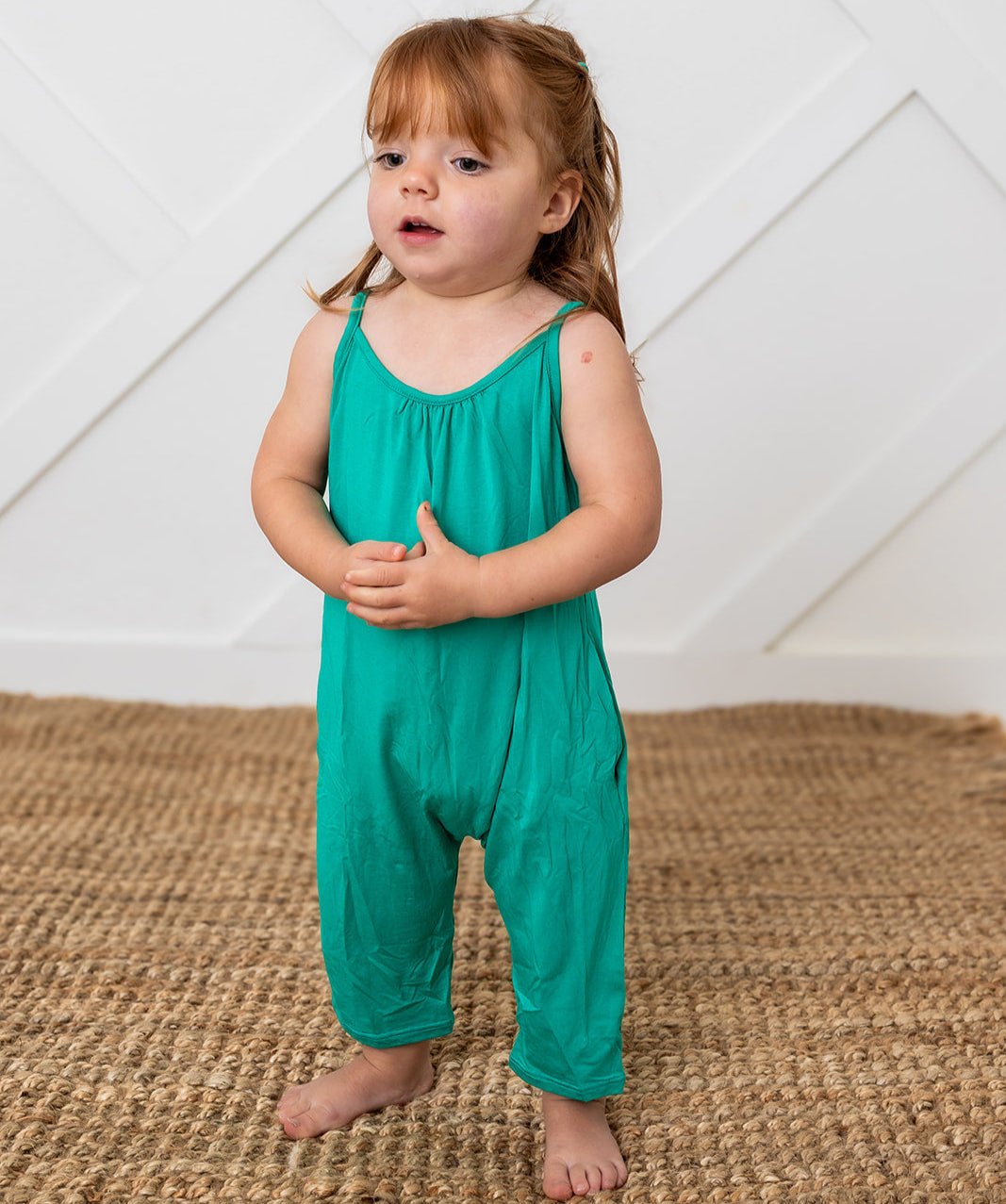 Emerald green toddler jumpsuit with pockets, worn by a barefoot child