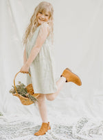 Sage green baby girl dress with pleats, embroidery, and button closure, worn by a young child model.