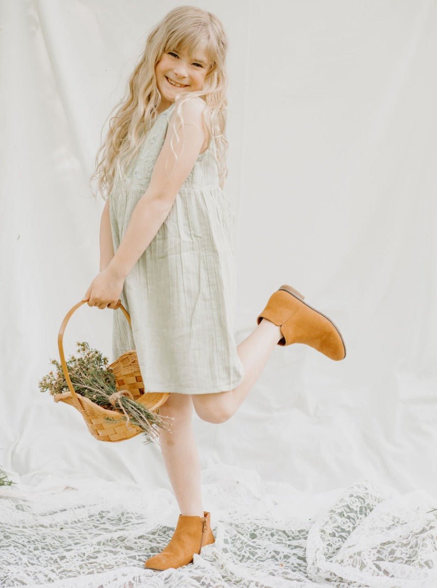 Sage green baby girl dress with pleats, embroidery, and button closure, worn by a young child model.