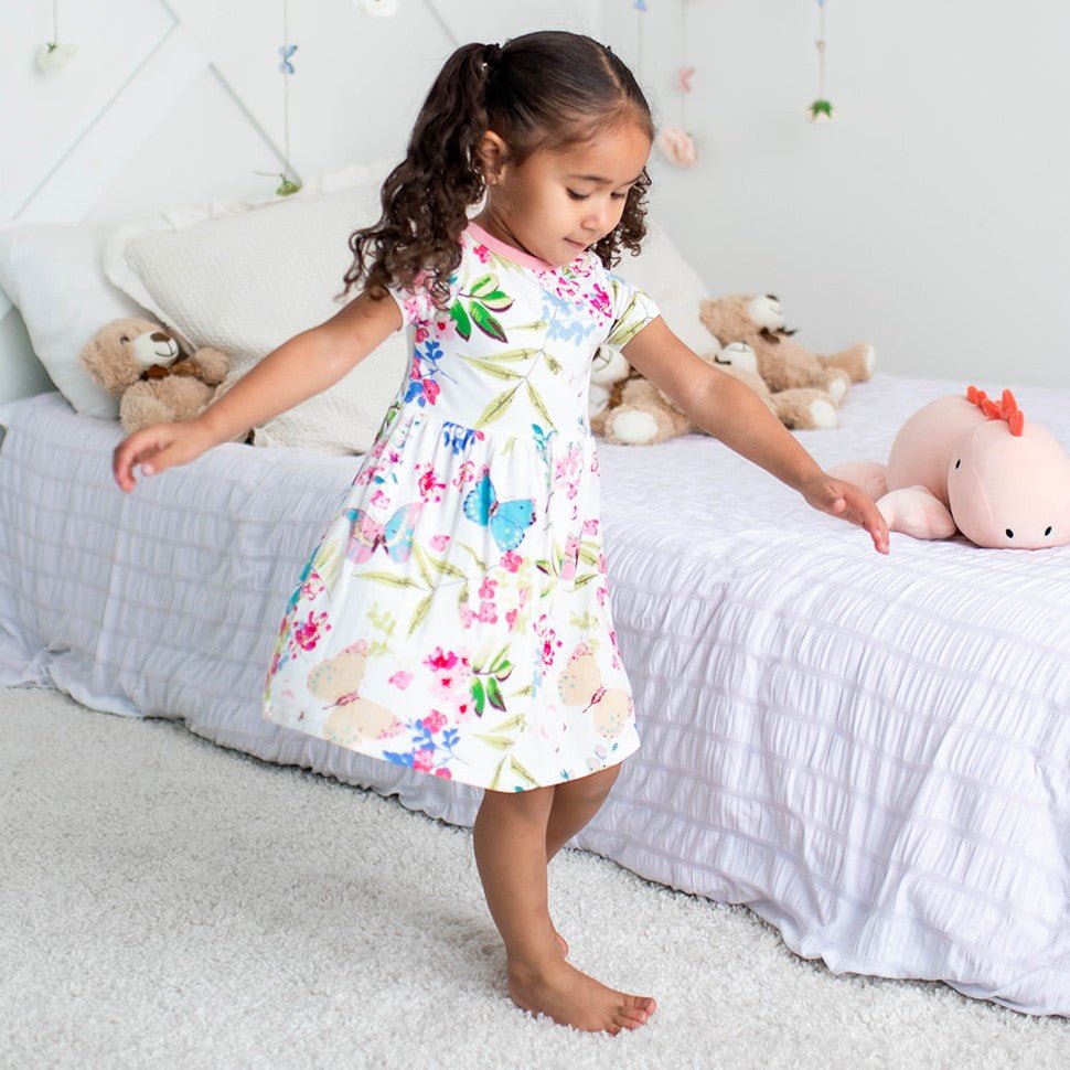 Pink short-sleeve toddler dress on a smiling child holding a teddy bear