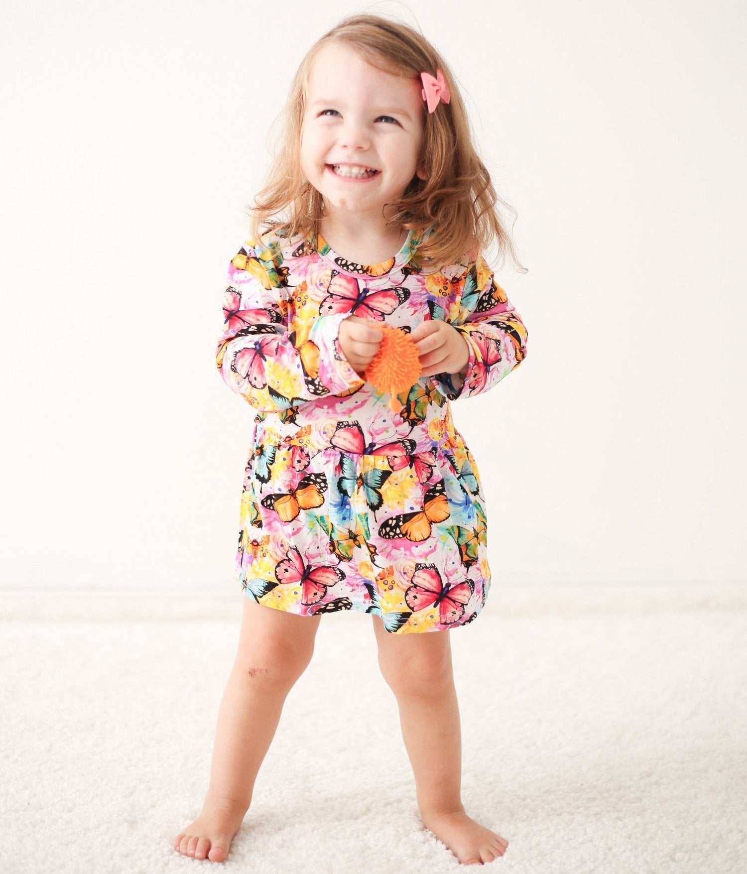 Flutter Dreams bodysuit dress with long sleeves in a pink flutter pattern on a child model
