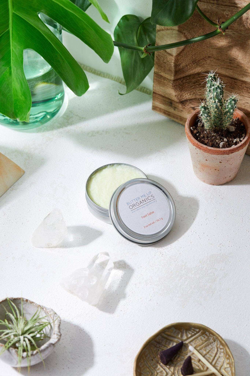 Hydrating Foot Salve in tin container on white surface with plants.