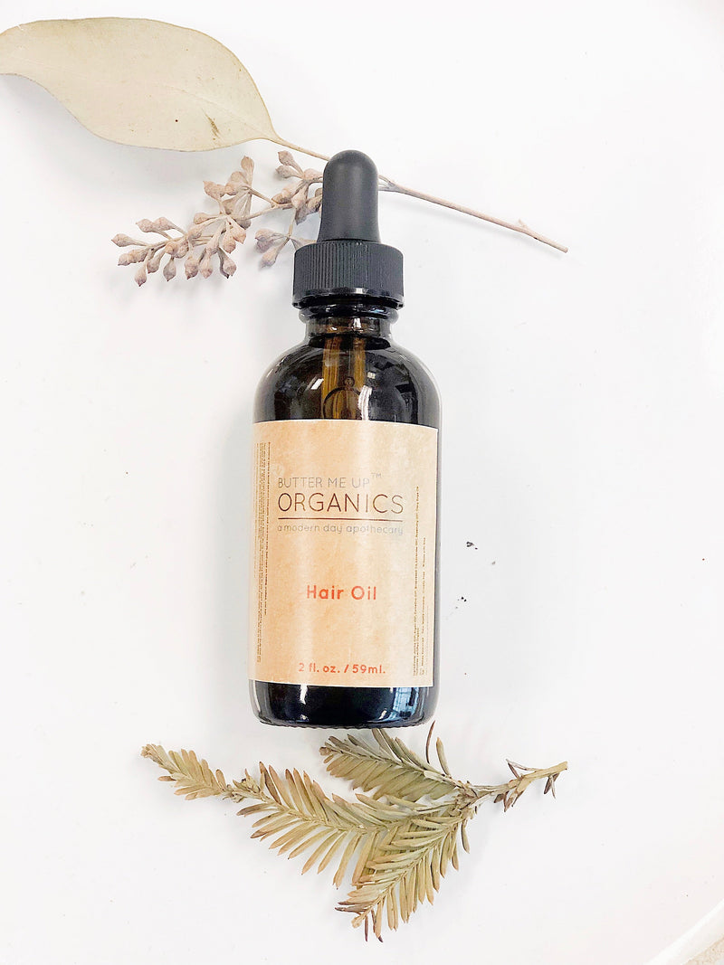 Organic Hair Oil in a 2oz glass bottle with dropper, made with Argan, Jojoba, and Camelina oils, surrounded by dried leaves.