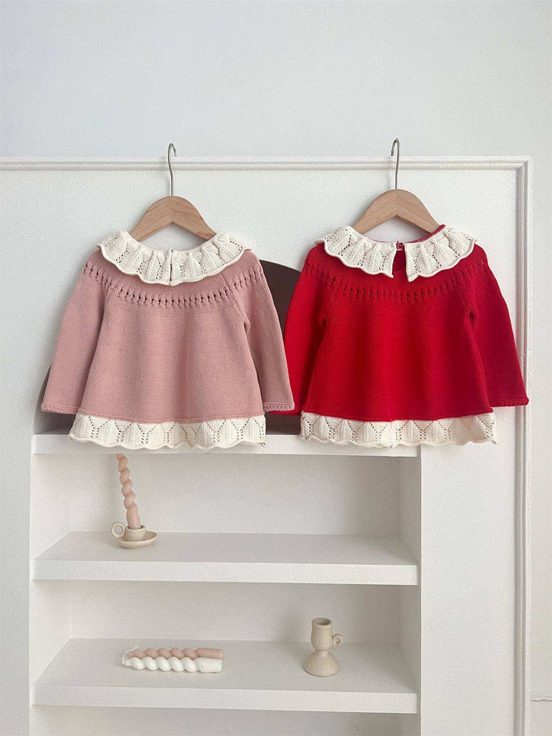 Girls' scalloped design tops in pink and red hanging on wooden hangers.