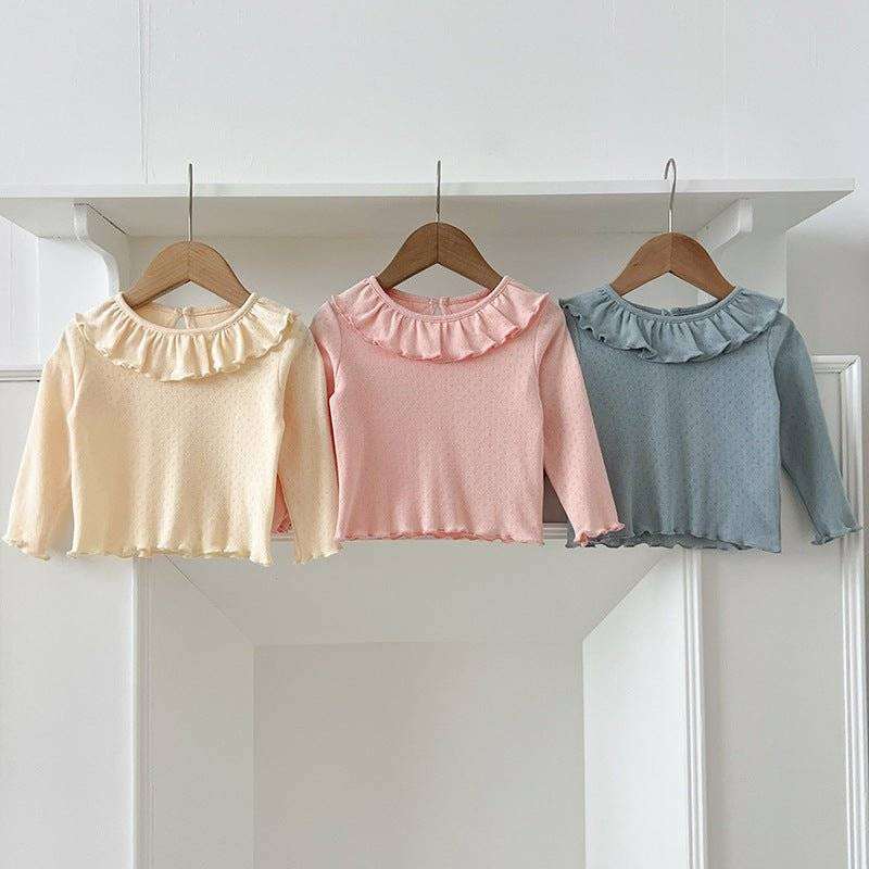 Girls soft comfortable long tops in cream, pink, and blue with ruffled neckline, hanging on hangers.