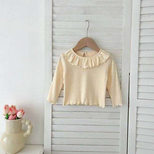 Girls soft comfortable long top with simple design and ruffled neckline hanging on a white shutter.