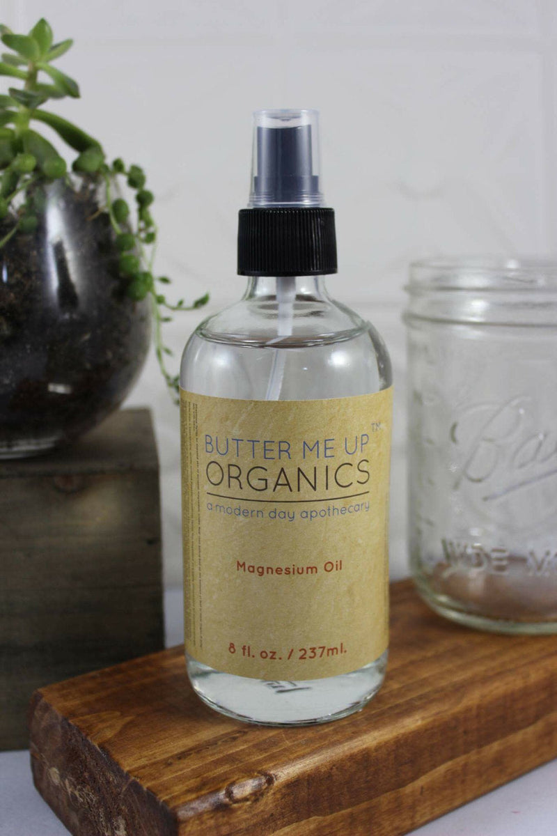 Magnesium oil spray bottle on wooden surface with glass jar and plant, promoting natural health benefits.