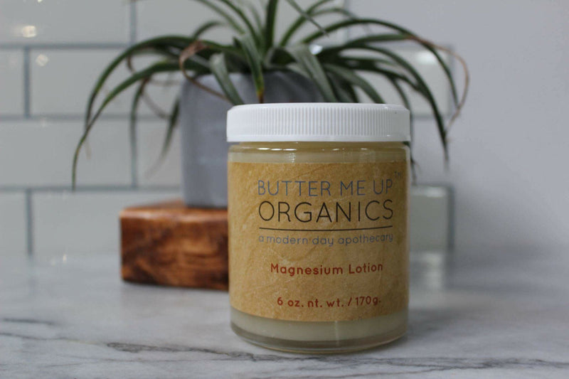 Organic Magnesium Lotion in a 6 oz glass jar with a white lid, on a marble countertop in front of a potted plant.