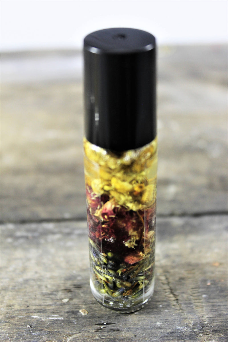 Organic essential oil perfume blend in roll-on bottle with chamomile, rose petals, and lavender suspended in oil.