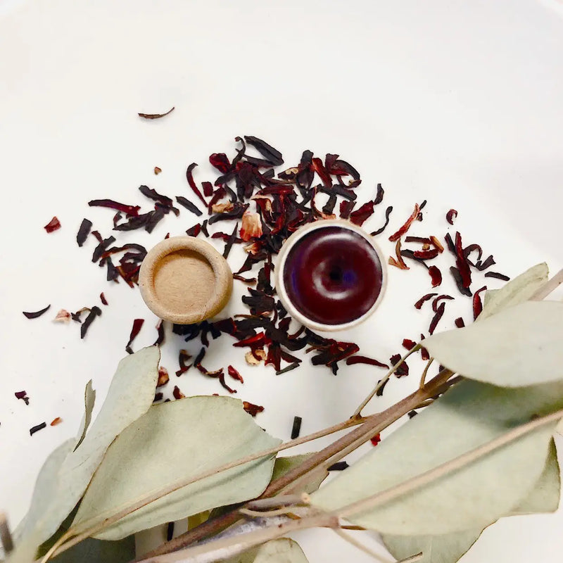 Organic natural cheek and lip stain in a paperboard tube, surrounded by dried botanicals.