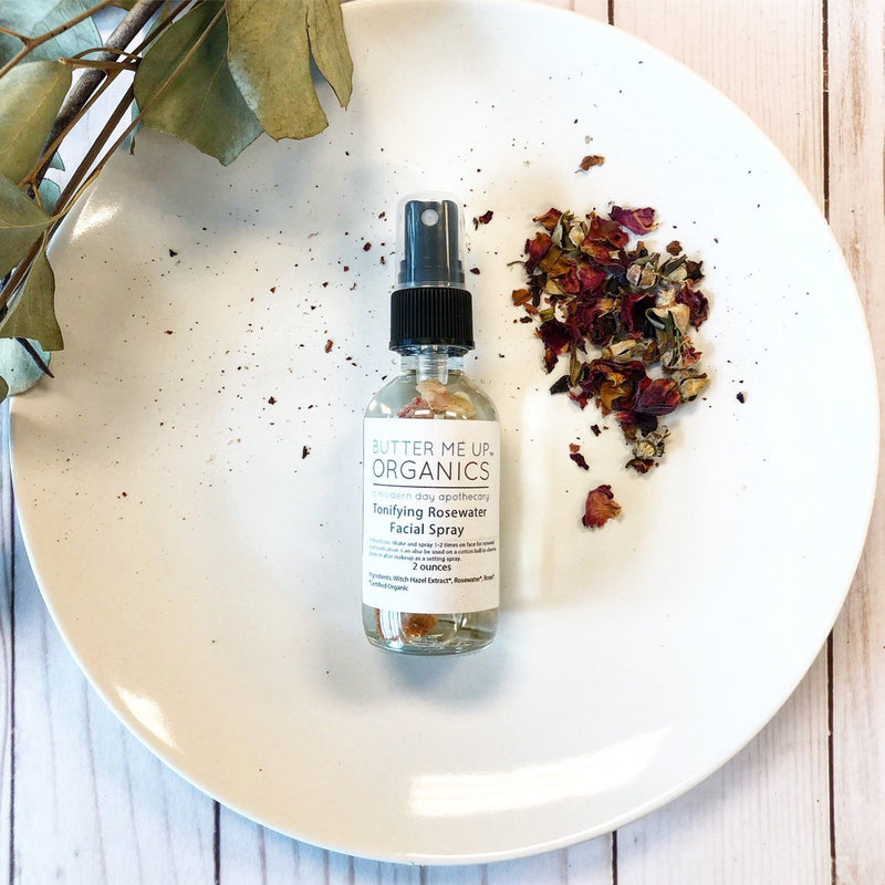 Organic rosewater toner and setting spray in a glass bottle on a white plate with rose petals.