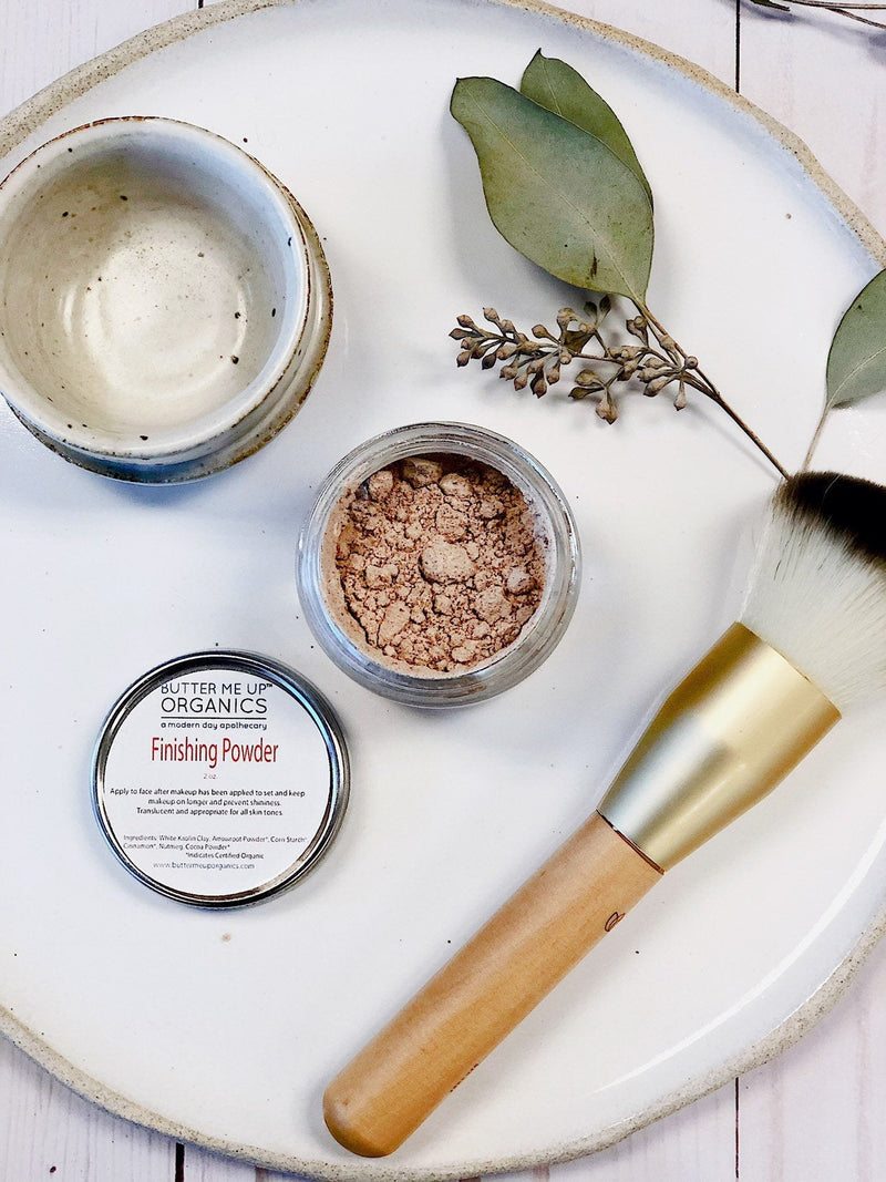 Organic finishing powder in a glass jar with metal lid, shown with a makeup brush on a plate.