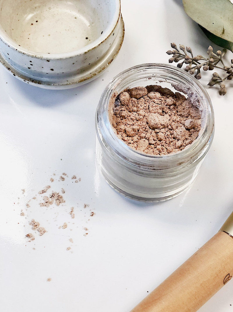 Organic finishing powder in a glass jar with metal lid on a white surface.