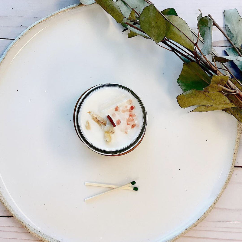 Organic soy space clearing candle with crystals on a plate, alongside matches and greenery.