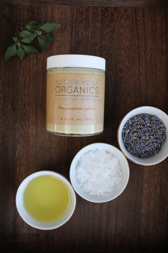 Organic Magnesium Lotion jar surrounded by lavender, salt flakes, and oil in bowls on a wooden surface.