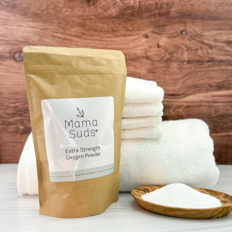 Extra Strength Oxygen Powder by Mama Suds in eco-friendly packaging with white towels and a bowl of powder on a wooden surface.