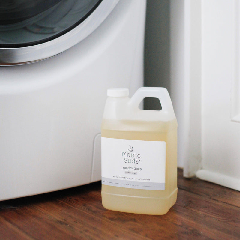 Laundry Detergent Soap by MamaSuds in a recyclable bottle placed beside a washing machine.