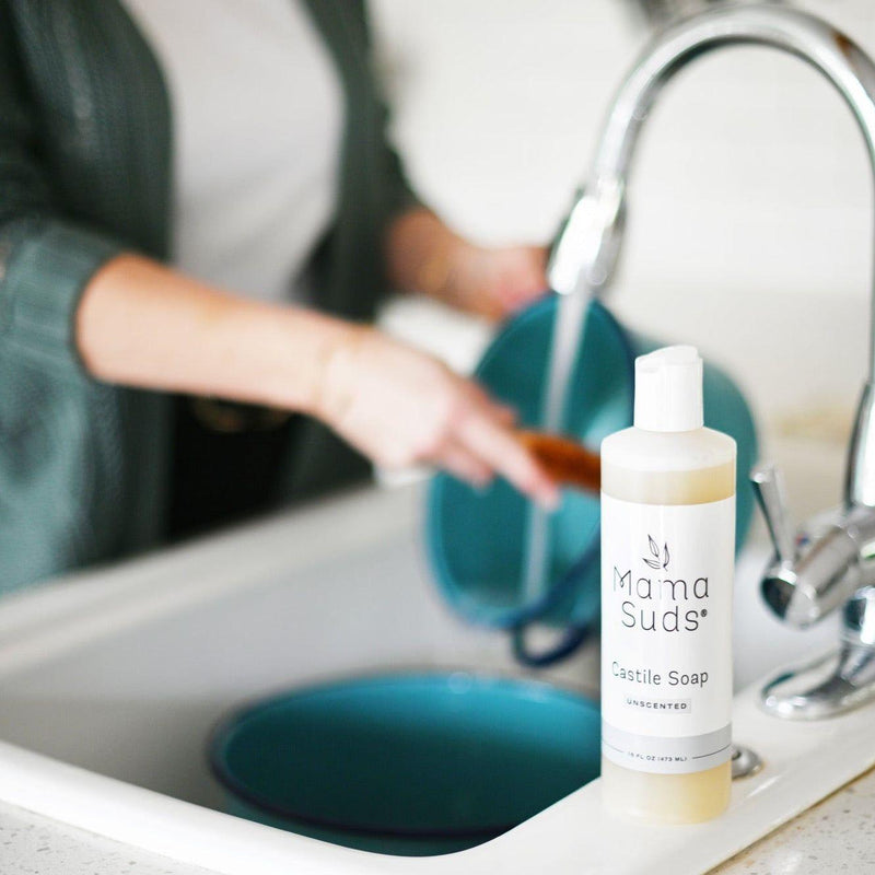 MamaSuds Castile Liquid Soap bottle on kitchen counter with person cleaning dishes.