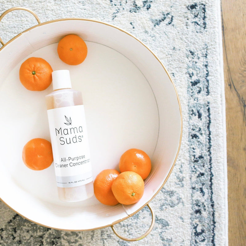 MamaSuds All-Purpose Cleaner Concentrate bottle in a tray with oranges, on a patterned rug.