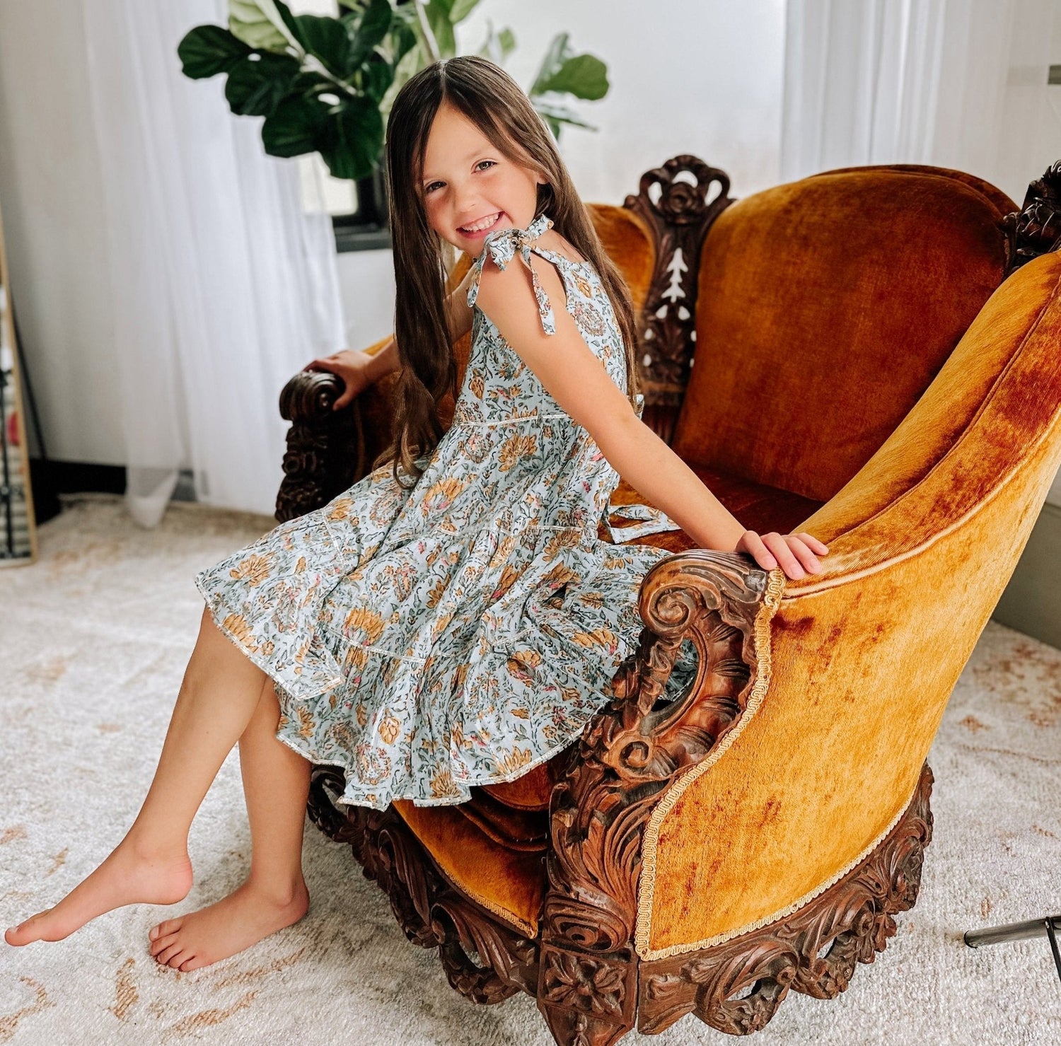 Baby blue floral dress with adjustable tie straps, shown on a smiling girl with long brown hair.