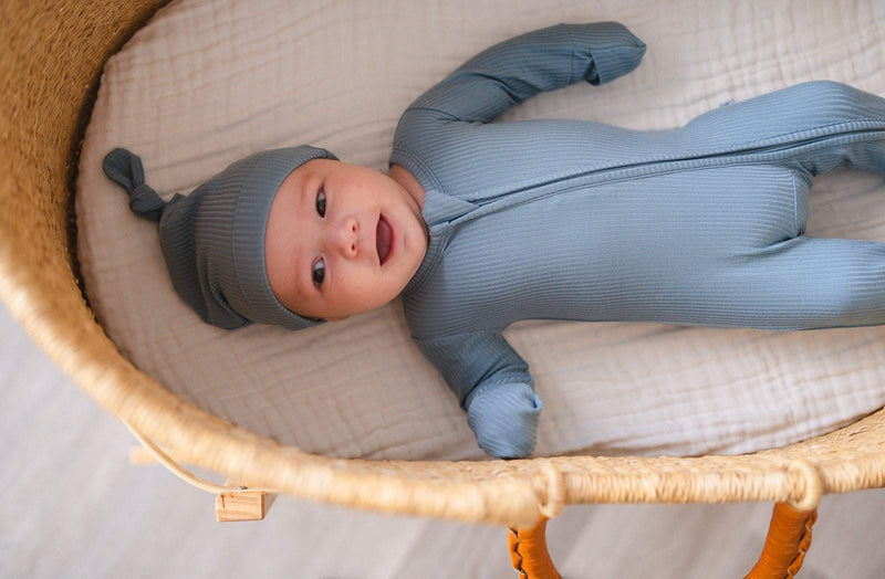 Newborn in cozy blue ribbed knot hat and matching outfit in a basket.