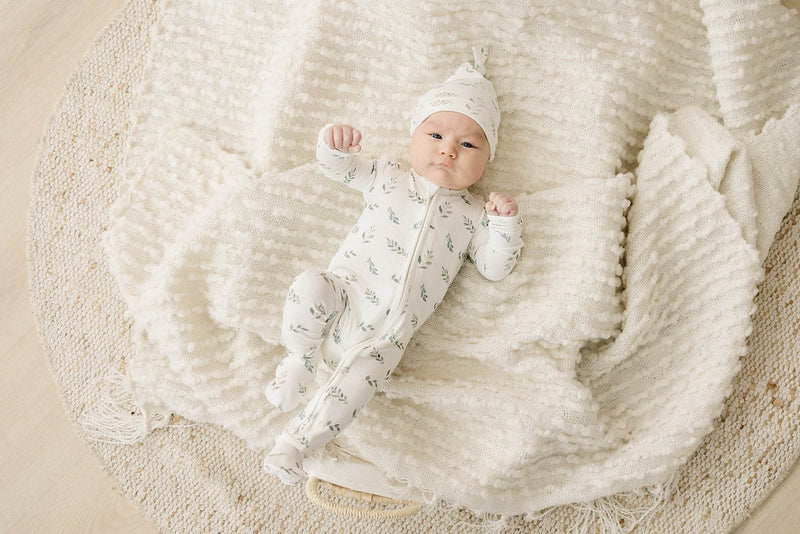 Newborn wearing green leaves knot hat, made from bamboo viscose and spandex, laying on a soft blanket.
