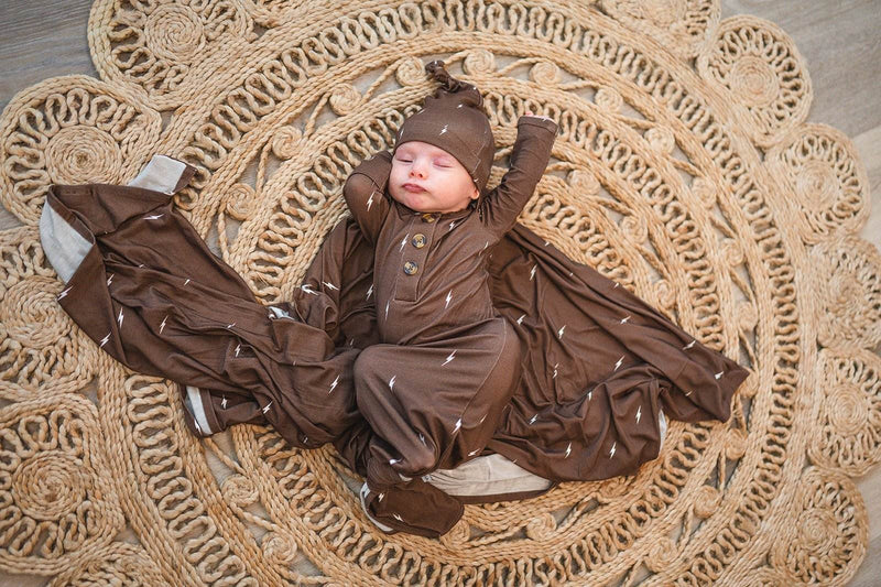 Brown lightning knotted baby gown with fold-over cuffs laid on a textured round mat, designed for comfort and style in bamboo fabric.