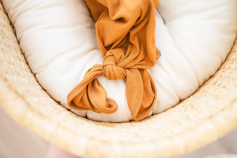 Caramel ribbed knotted baby gown in a cozy wicker basket.
