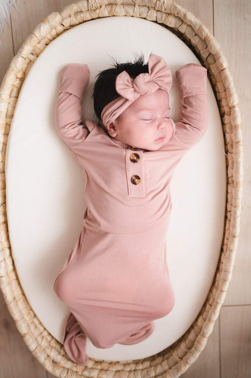 Knotted baby gown in dusty pink on infant, featuring bamboo viscose and fold-over cuffs.